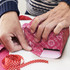 A pair of hands wrapping a gift in vibrant pink personalised gift wrapping paper, with red polka dot ribbon nearby.