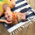 A striped navy and white cotton towel lies on a wooden surface, with a woman relaxing, headphones, phone, and sunglasses nearby.