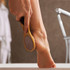 A wooden pedicure tool with a textured surface, being used on a bare foot.