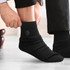 Black socks being worn, featuring a subtle logo on the side. The person is adjusting them while seated.
