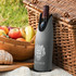 A drink bottle cooler in grey features a logo and is positioned next to a woven basket filled with fruits.