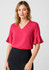 A woman wearing a pink fluted sleeve blouse with a V-neckline, paired with a black skirt. The image features a brand logo.