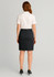 A woman in a white polo shirt and dark mid waist stretch chino skirt, facing away from the camera.