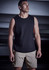 A man wearing a black sleeveless top and beige sports shorts stands in a dimly lit setting. The shorts feature a logo.