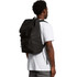 A black recycled field backpack worn over a person's shoulder, featuring adjustable straps and a simple design.