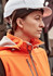 An orange women's softshell jacket with a zipper, worn by a woman in a white hard hat.