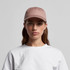 A light brown cap with a flat brim and a logo, worn by a woman in a white t-shirt.