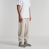 A person wearing beige track pants paired with a white t-shirt and grey sneakers, with the pants featuring a logo.
