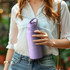 A drink bottle in soft lavender, featuring a handle and logo, held by a person wearing a white shirt and denim jeans.