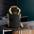 A drink bottle cooler bag in black with a tan handle and adjustable strap, featuring a logo.