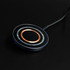 A round, black and silver wireless charger with a copper centre and a textured cable connected.