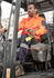An orange water-resistant hoodie is worn by a man operating machinery, with segmented tape detail on the sleeves.