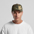 A soft camo cap in shades of green and brown, featuring a structured design and a logo on the front.