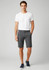 A model wearing grey dress shorts paired with a white t-shirt and navy shoes, featuring a branding logo.