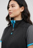 A woman models a black vest with blue accents, featuring a stand-up collar and a zipper. The vest has a logo.