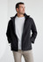 A man wearing a black rain jacket with a grey shirt underneath. The jacket has a logo on it.
