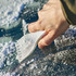 A white ice scraper being used to remove snow from a car windscreen, with a gloved hand gripping the scraper.