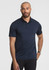 A man stands wearing a navy blue short sleeve polo shirt, featuring a collar and a logo.
