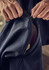 A close-up of hands zipping a navy softshell jacket with a contrasting inner layer. The jacket features a logo.