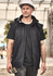 A unisex black softshell jacket features a hood, zippered pockets, and a branding logo, worn by a man at a construction site.