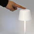 A white rechargeable table lamp with a tapered design, being turned on by a hand pressing the top.