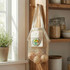 A small, cream-coloured cotton mesh tote bag hangs on a hook, holding a few onions. It features a logo on the front.