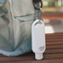A white carabiner sunscreen bottle in a 50ml size, attached to a bag. The product features a small, sleek design.