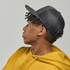A black trucker cap with a mesh back, worn by a person in a mustard yellow hoodie.
