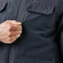 A close-up of a navy jacket featuring a zippered chest pocket and front flap pockets, held by a person's hand.