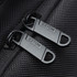 Close-up of black zippers with a branding logo on a textured fabric, part of the Exton Laptop Backpack.
