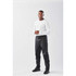 A man stands wearing black rain pants and a white long-sleeve shirt. The pants have a logo on them.
