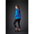 A woman stands sideways wearing a blue lightweight softshell jacket and black leggings, set against a dark background.