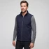 A man wearing a navy blue softshell vest over a grey long-sleeve shirt, with a zipper and side pockets.