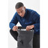 A person in a blue fleece jacket inspects the interior of a black backpack. The backpack features a logo.