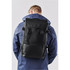 A black backpack with adjustable straps is worn on the back of a person, who is facing away from the camera.