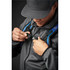 A person fastening a strap on a black backpack with blue accents while wearing a grey jacket and cap.