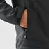 A black softshell jacket with a zippered pocket, featuring a hand reaching inside the pocket.
