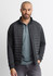 A men's tailored jacket in black, featuring a zip front and quilted detailing, worn over a green polo shirt.