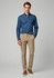 A man wearing a blue shirt and beige chinos, standing against a neutral background. The pants have a branding logo.