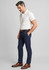A man in a beige polo shirt and navy chinos stands, wearing brown dress shoes and a belt, with a subtle logo visible.