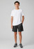 A model wearing black sports shorts and a white t-shirt, standing with hands in pockets. The shorts feature a logo.