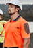 An orange short sleeve polo shirt featuring a logo and black striped design, worn by a man in a hard hat.