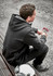 A unisex zip front hoodie in black, featuring multiple pockets, worn by a seated person on a construction site.