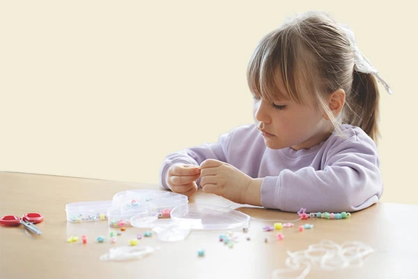 Young girl threading colourful beads onto string at a classroom table