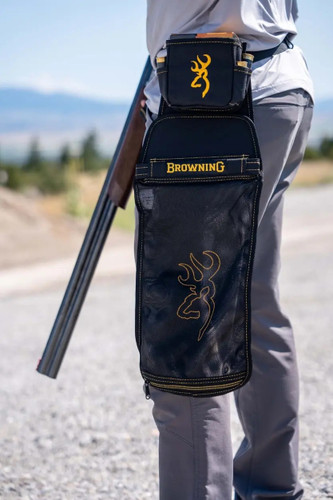 A shooter wearing a black mesh hull bag on a belt while holding a shotgun outdoors