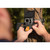 Close-up of hands inserting the lithium battery pack into a trail camera mounted outdoors on a tree