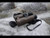 A pair of tan Bushnell Forge binoculars with a neck strap resting on rugged gray rocks outdoors