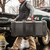Person carrying a black Pelican Vault V700 hard case outdoors next to a vehicle in a lifestyle setting
