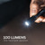 Close-up view of the flashlight beam illuminating a dark space with an informative overlay reading 100 LUMENS