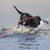 A black hunting dog splashing and retrieving through open water with an orange floating check cord trailing behind